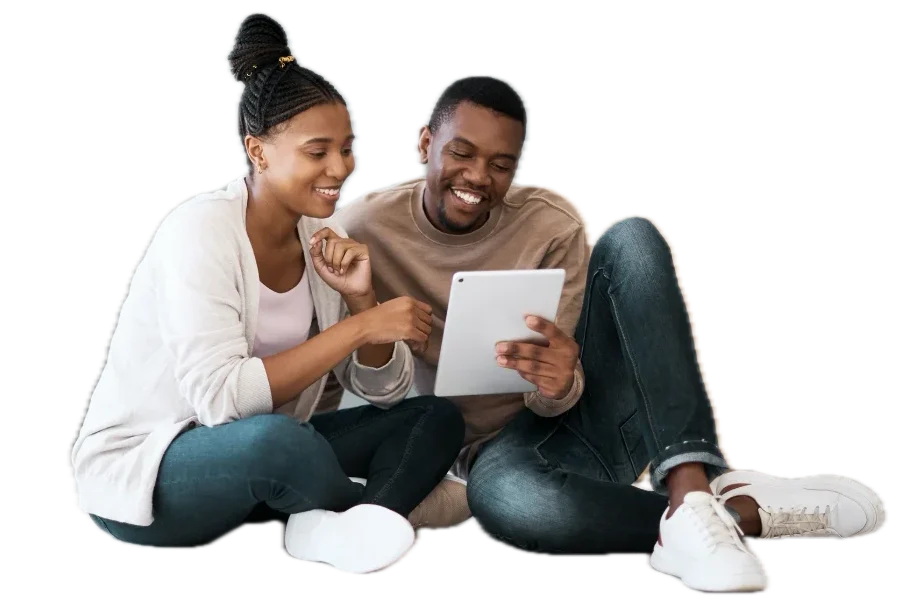 Smiling couple sitting on floor, looking at a tablet together.
