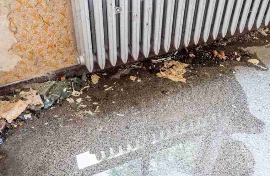 Contaminated water near a radiator with visible debris and wall damage, representing gray water.