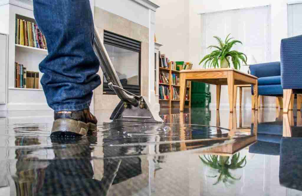 Person walking through a flooded living room caused by clean water from a broken pipe. This type of drying illustrate the purpose of water mitigation.