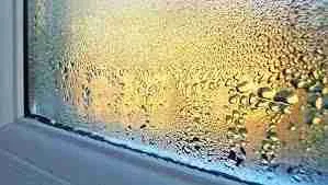 Condensation on a windowpane with humidity, illuminated by warm light from outside.