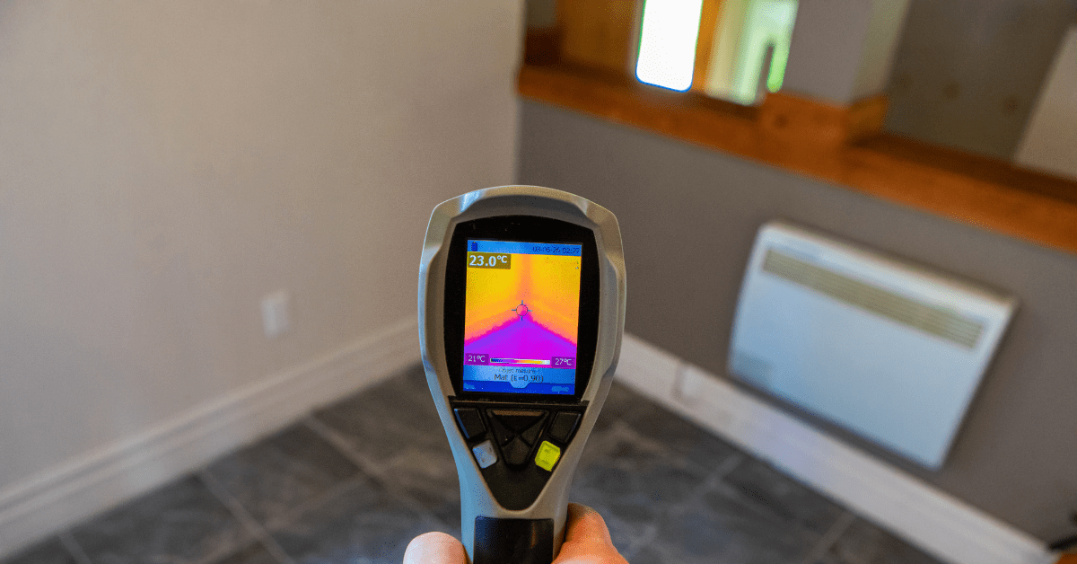 A hand holds a thermal imaging device used for indoor air quality or moisture testing inside a residential room.