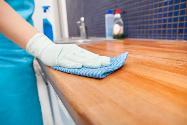 Person wearing a glove wiping a kitchen countertop with a cloth to maintain cleanliness and prevent mold buildup.