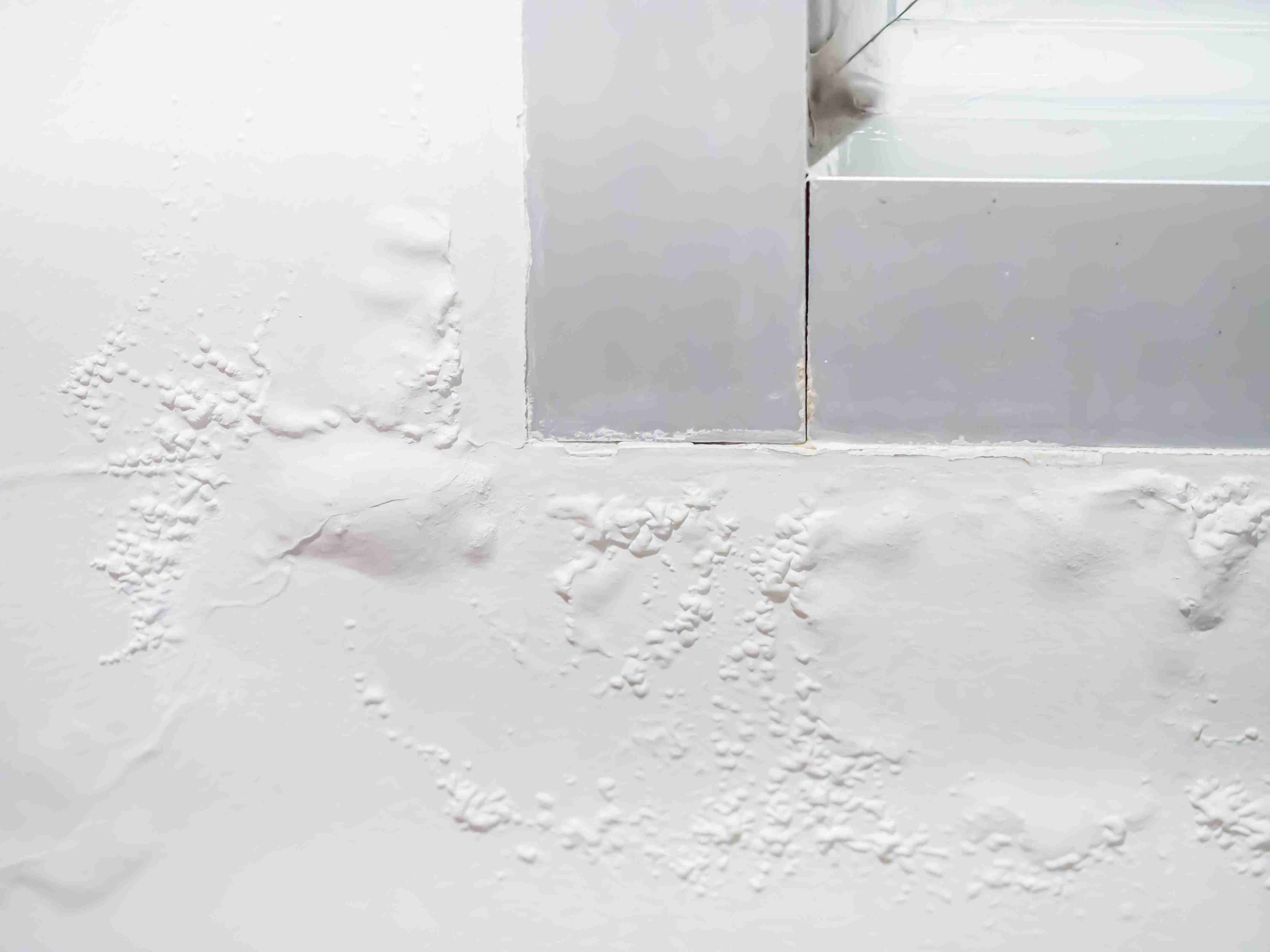 Close-up of a wall with bubbling and peeling paint near a window, showing signs of moisture damage.