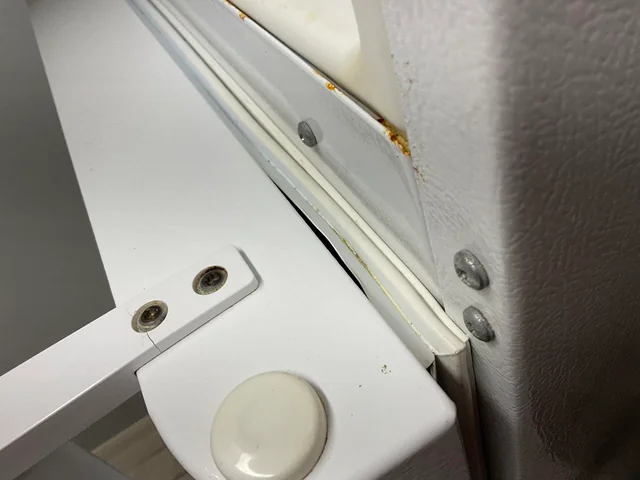 Refrigerator door hinge with visible rust and misalignment near the gasket seal.