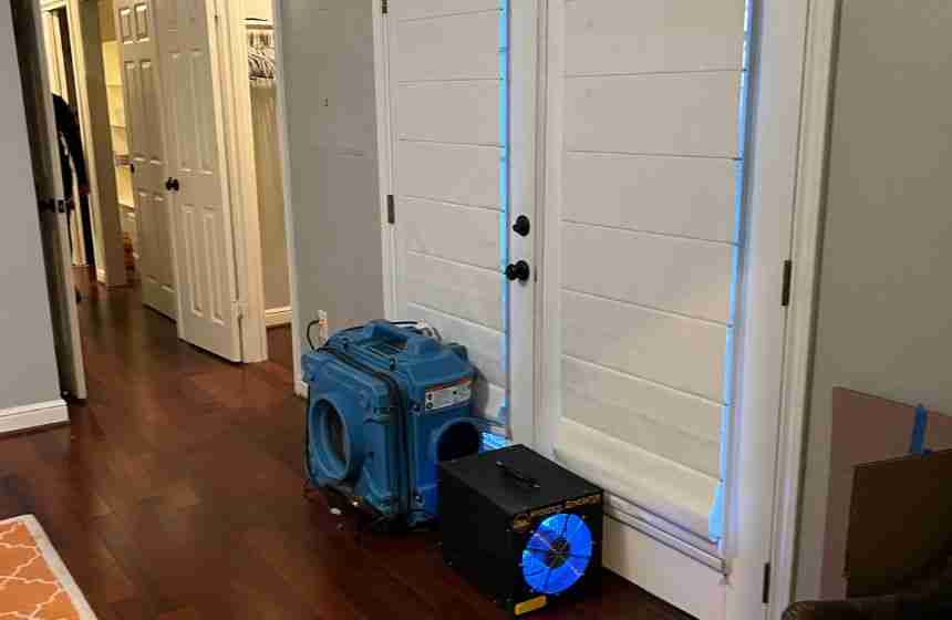 Water restoration equipment in use inside a Waller, TX home, showing air movers and dehumidifiers set up near a patio door on hardwood floors to dry out water damage.