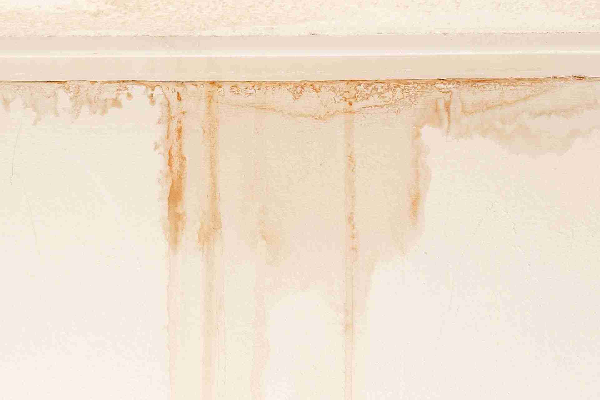 Wall with visible brown water stains and discoloration near the ceiling, indicating moisture damage or a possible leak.