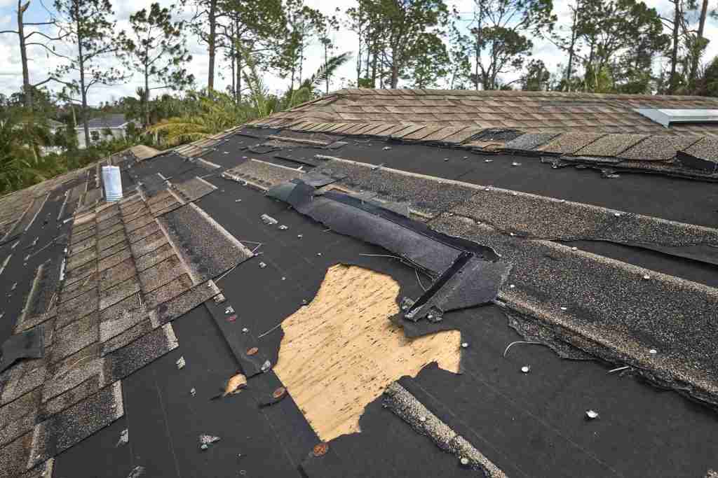 Asphalt shingle roof with visible storm damage and missing shingles exposing the wooden roof deck.