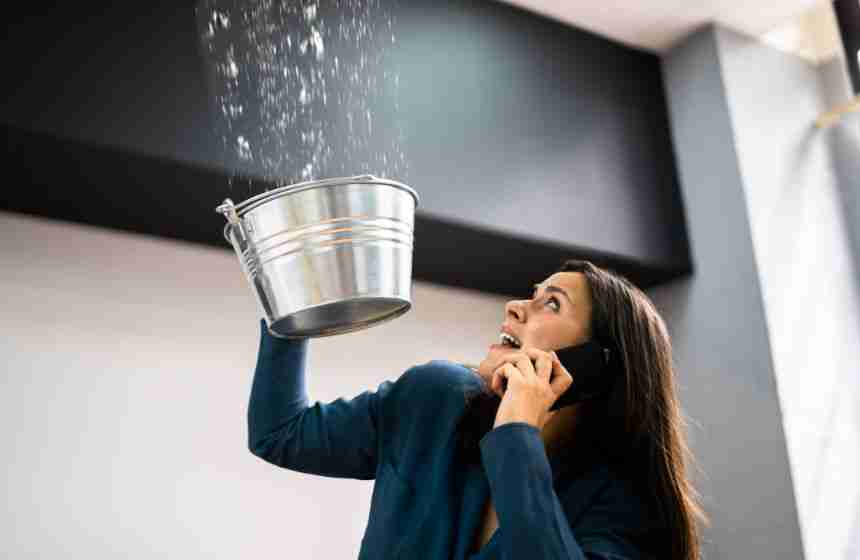 Panicked woman in Waller, TX holding a bucket under a leaking ceiling while calling for water damage mitigation services.