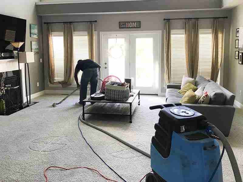 Technician extracting water from carpet in a living room after flooding
