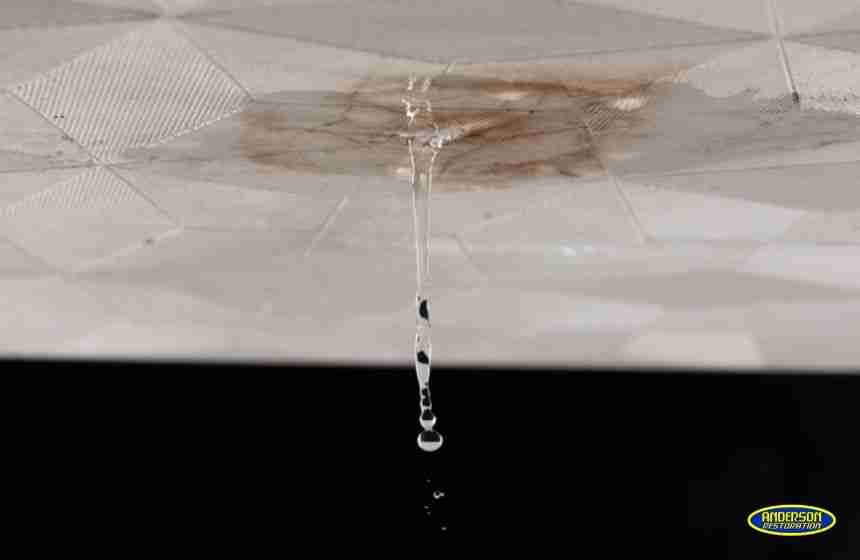 Close-up of a leaking ceiling tile with water dripping down, showing significant staining and damage—an example of a property in need of water damage restoration in The Woodlands, TX.