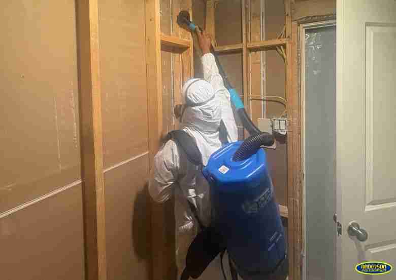 Technician in protective gear scrubbing mold from wooden wall studs inside a home in Houston, Texas. from Anderson Restoration LLC in Houston, TX