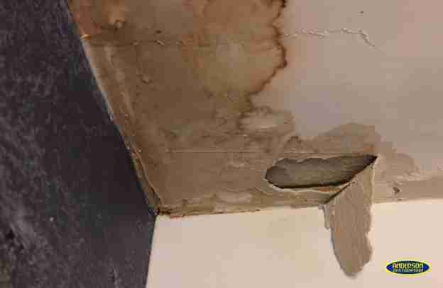 Water-damaged ceiling with visible brown stains, peeling paint, and a hole caused by moisture exposure in a home near College Station, TX.