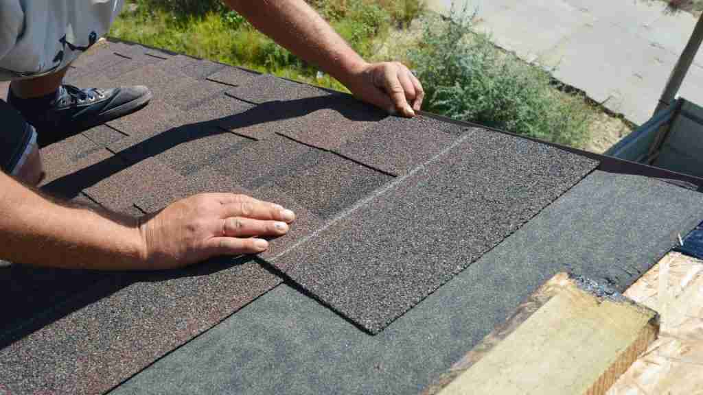 Anderson Restoration crew installing new asphalt shingles on a residential roof in a Houston suburb, tools and materials staged on the roof