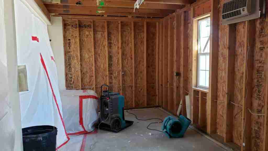 Restoration technician removing wet baseboards in a Houston-area bathroom with a moisture meter reading visible on adjacent drywall