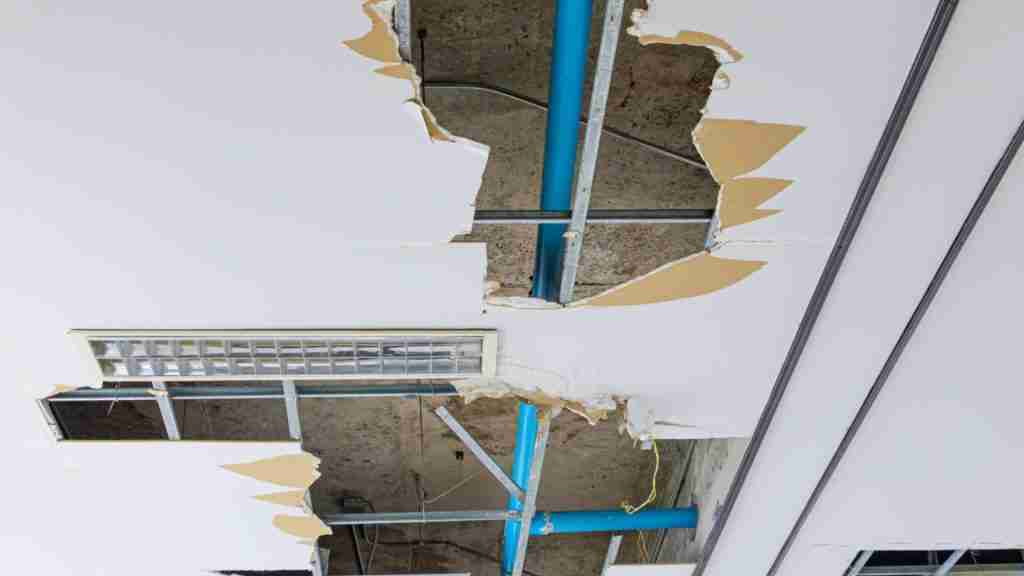 Water-stained ceiling in a residential living room caused by an upstairs bathroom leak, with visible discoloration and slight bubbling in paint