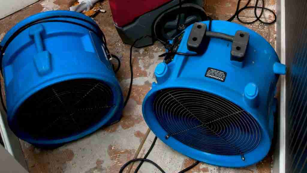 Restoration technician positioning air movers under kitchen cabinets with toe kicks removed to facilitate subfloor drying
