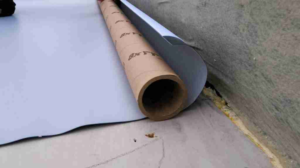 Roofing technician rolling white silicone coating onto a commercial flat roof on a sunny day, with HVAC units and parapet walls visible in the background