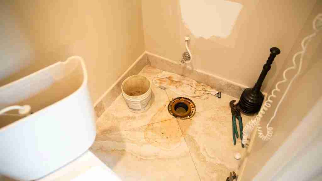 Restoration crew in full PPE extracting contaminated water from a residential bathroom with commercial pump equipment visible
