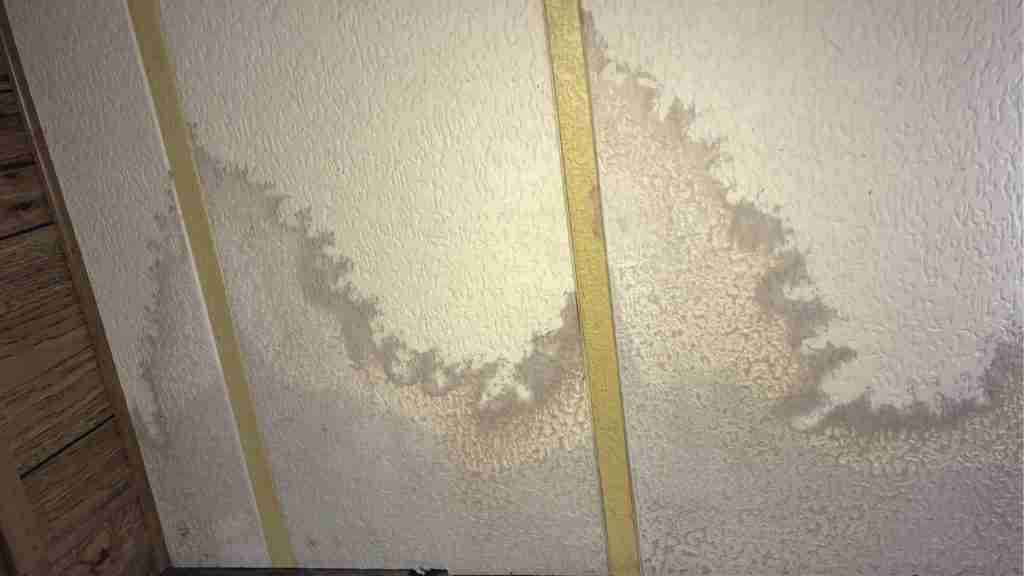 Residential wall with bubbling paint and visible water stain running vertically from ceiling line to baseboard in a Houston-area home