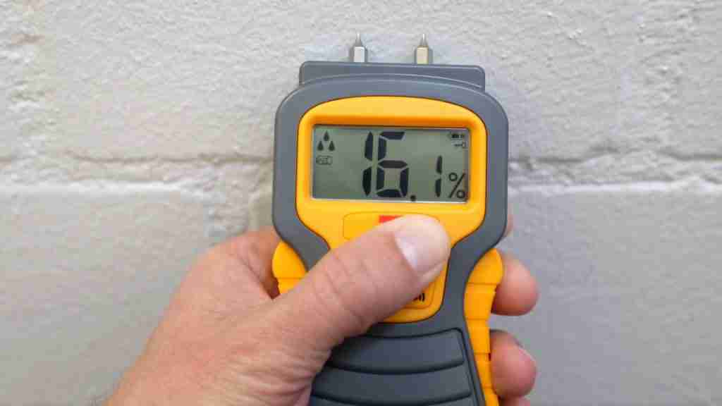 Technician using a pin-less moisture meter on laminate flooring near a kitchen transition strip, with moisture reading display visible