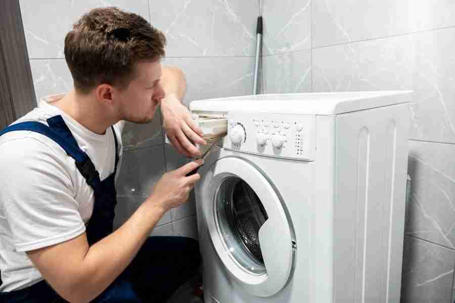 Technician kneeling beside a front loading washing machine inspecting hose connections in a Houston home