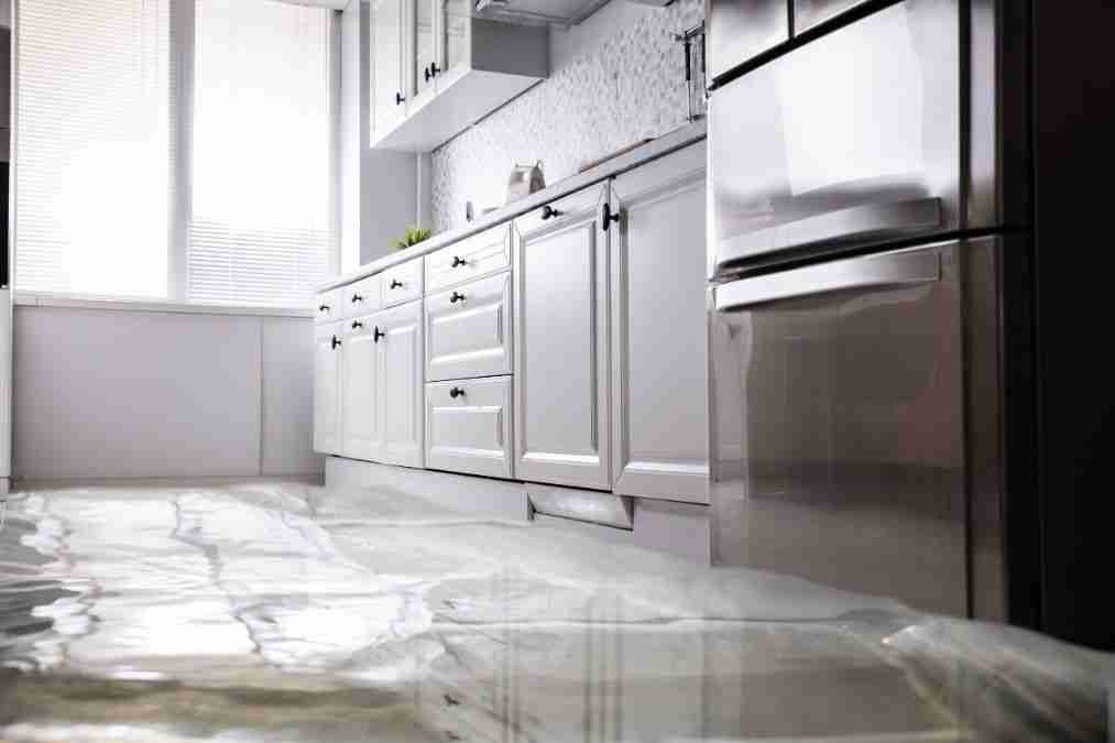 Stainless steel refrigerator beside white cabinets with water flooding the kitchen floor