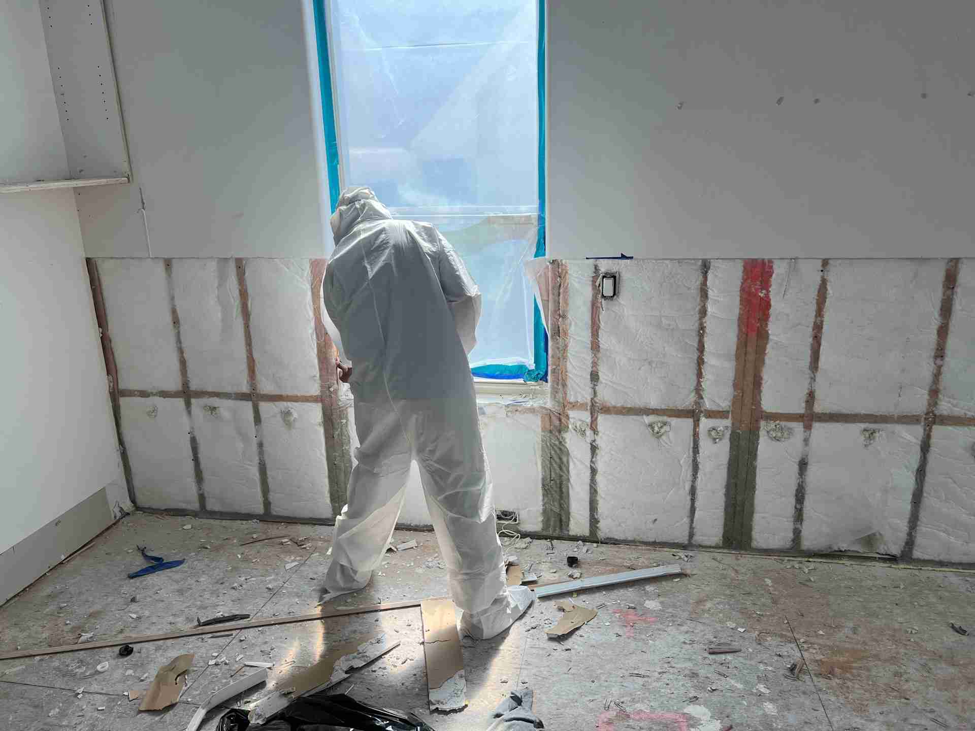 Restoration technician in full PPE removing drywall during mold remediation in Bellaire TX