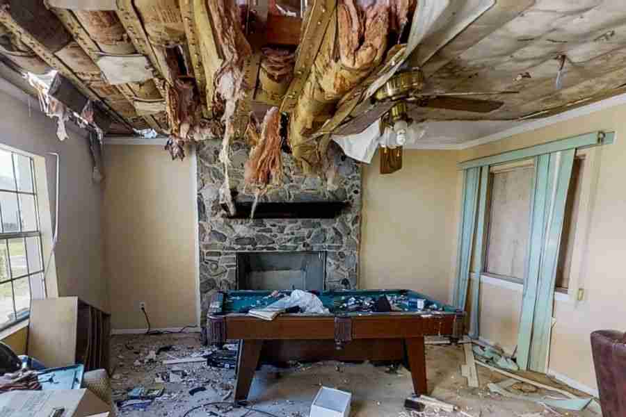 Living room with a collapsed ceiling, hanging insulation, and debris scattered across furniture and floor